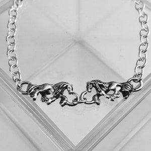 May include: Silver chain bracelet with three horse charms. The bracelet is displayed in a clear plastic box.