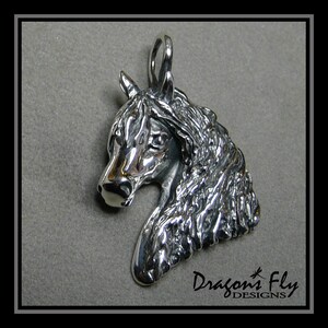 May include: Silver pendant featuring a detailed, three-dimensional sculpture of a horse's head. The horse's mane is textured and flowing. The pendant has a loop at the top for attaching a chain.