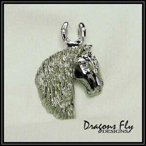 May include: Silver horse head pendant with a horseshoe charm. The horseshoe has small clear stones set into it. The pendant is a detailed design with a textured finish.