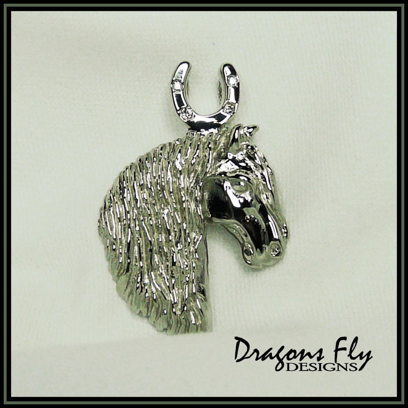 May include: Silver horse head pendant with a horseshoe charm. The horseshoe has small clear stones set into it. The pendant is a detailed design with a textured finish.