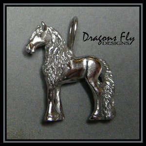 May include: Silver charm of a horse with a long mane and tail. The charm is standing on all four legs and has a loop at the top for attaching to a necklace or bracelet. The charm is made by Dragons Fly Designs.
