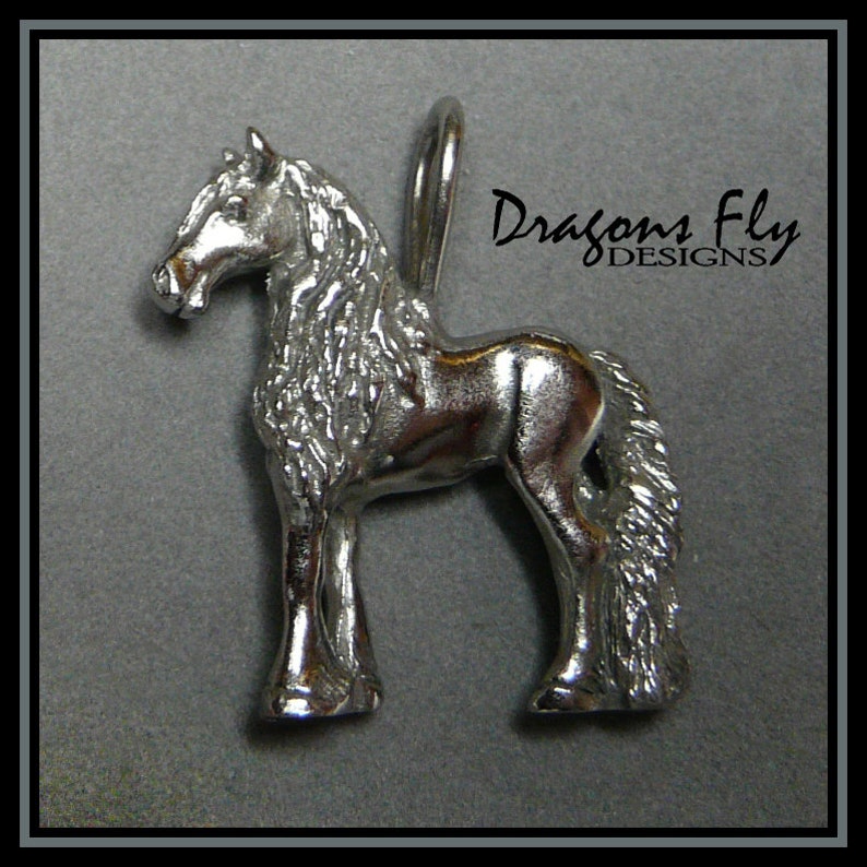 May include: Silver charm of a horse with a long mane and tail. The charm is standing on all four legs and has a loop at the top for attaching to a necklace or bracelet. The charm is made by Dragons Fly Designs.
