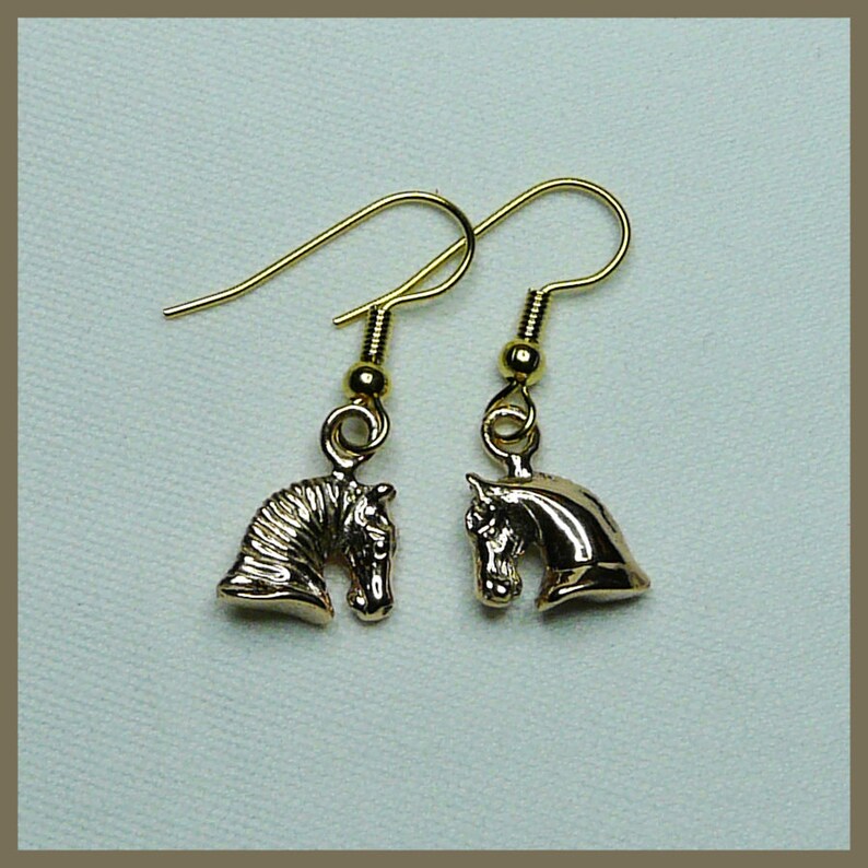 May include: A pair of gold-tone earrings featuring a horse head design. The earrings are dangle style with a simple hook closure.