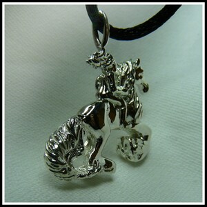 Peut inclure: Un collier avec un pendentif en argent repr&eacute;sentant une sculpture d&eacute;taill&eacute;e d'une personne &agrave; cheval. Le pendentif est attach&eacute; &agrave; un cordon noir.