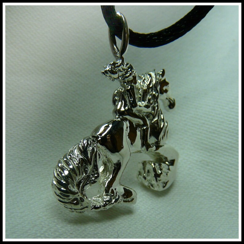 Peut inclure: Un collier avec un pendentif en argent repr&eacute;sentant une sculpture d&eacute;taill&eacute;e d'une personne &agrave; cheval. Le pendentif est attach&eacute; &agrave; un cordon noir.