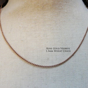 May include: A rose gold vermeil 1.3mm wheat chain necklace on a white fabric background.
