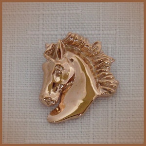 Pode incluir: Um pingente de cabe&ccedil;a de cavalo dourado com uma crina detalhada e um acabamento liso e polido.