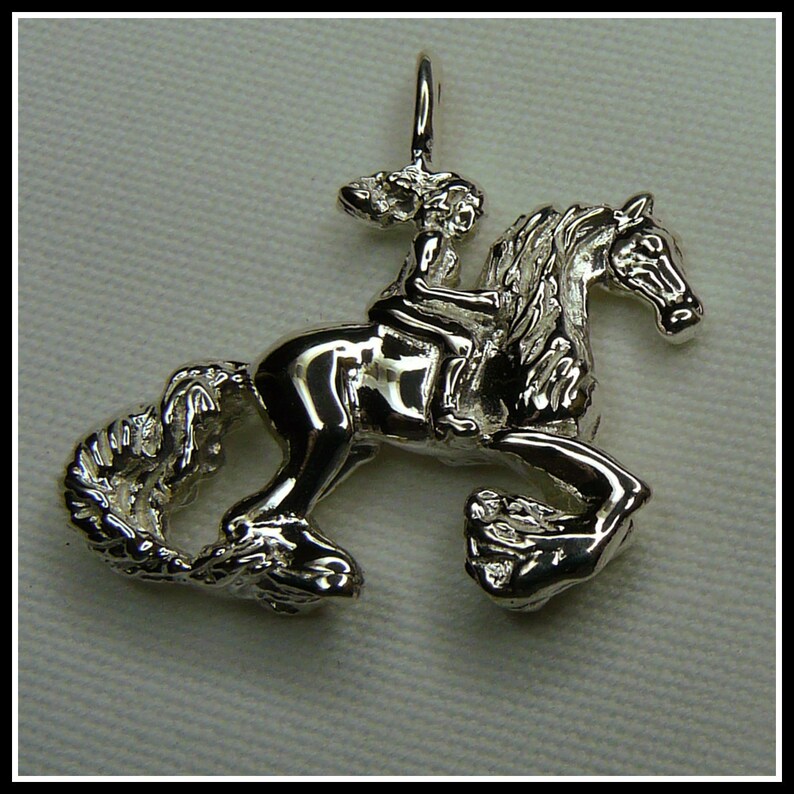 Peut inclure: Un pendentif en argent repr&eacute;sentant une fille &agrave; cheval. Le cheval se cabre sur ses pattes arri&egrave;re et la fille tient les r&ecirc;nes. Le pendentif est d&eacute;taill&eacute; et a une finition brillante.
