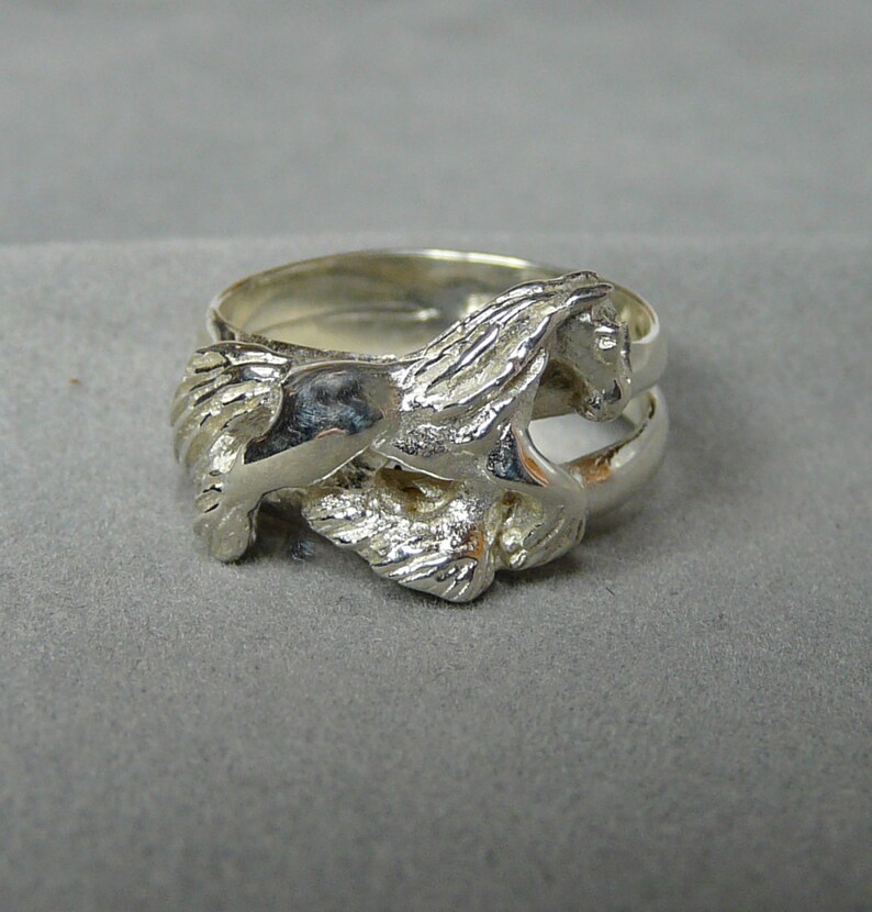 May include: A silver ring with a detailed design of a horse running. The ring is made of two bands, one on top of the other.