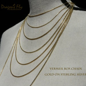 May include: A set of gold vermeil box chains of varying lengths, displayed on a white mannequin. The chains are made of gold on sterling silver. The text "VERMEIL BOX CHAIN GOLD ON STERLING SILVER" is displayed at the bottom of the image.