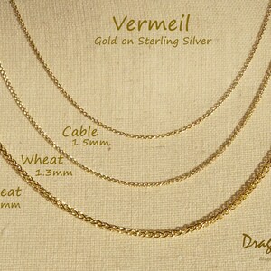 May include: Three gold chains of different widths and styles, labelled "Wheat 2.4mm", "Wheat 1.3mm", and "Cable 1.5mm". The chains are on a beige fabric background. The text "Vermeil Gold on Sterling Silver" is at the top of the image. The text "Dragon's Fly Designs" is at the bottom of the image.