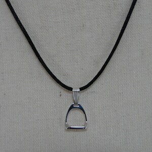May include: A silver stirrup pendant necklace on a black cord.