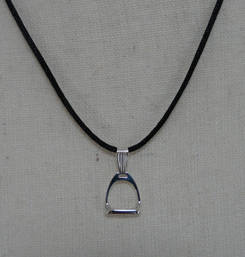 May include: A silver stirrup pendant necklace on a black cord.