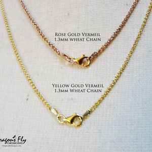 May include: Two gold chains, one rose gold and one yellow gold, both 1.3mm wheat chains. The chains are displayed on a white fabric background.