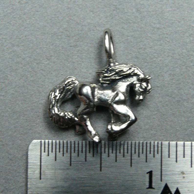 Peut inclure: Breloque en argent repr&eacute;sentant un cheval avec la t&ecirc;te tourn&eacute;e sur le c&ocirc;t&eacute; et la queue flottant derri&egrave;re lui. Le breloque mesure environ 2,5 cm de haut.