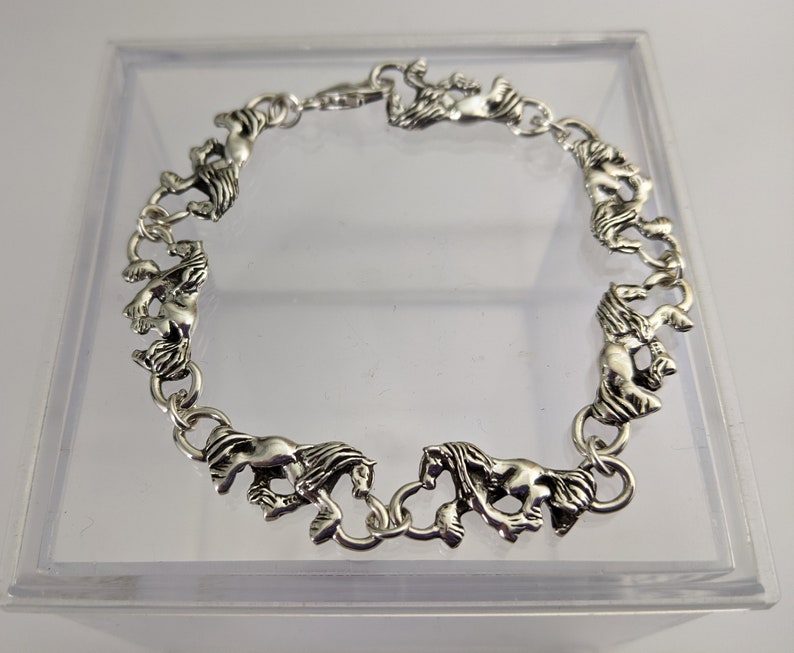 May include: Silver bracelet with a chain of linked horse figures.