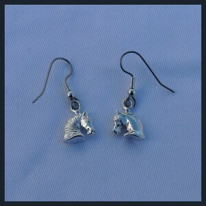 May include: A pair of silver dangle earrings featuring a horse head design. The earrings are on a white background.