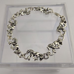 May include: A silver bracelet with a chain design featuring horse head charms. The bracelet is displayed in a clear plastic box.