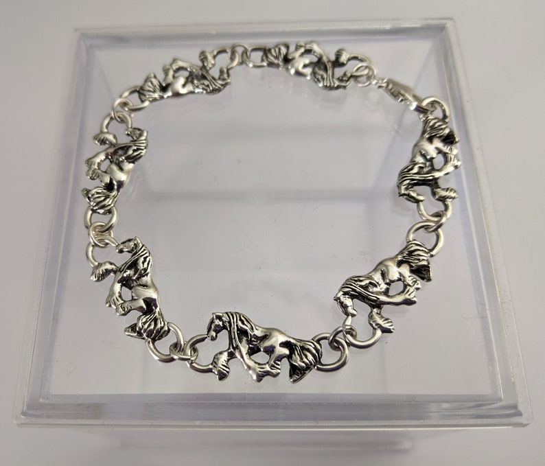 May include: A silver bracelet with a chain design featuring horse head charms. The bracelet is displayed in a clear plastic box.