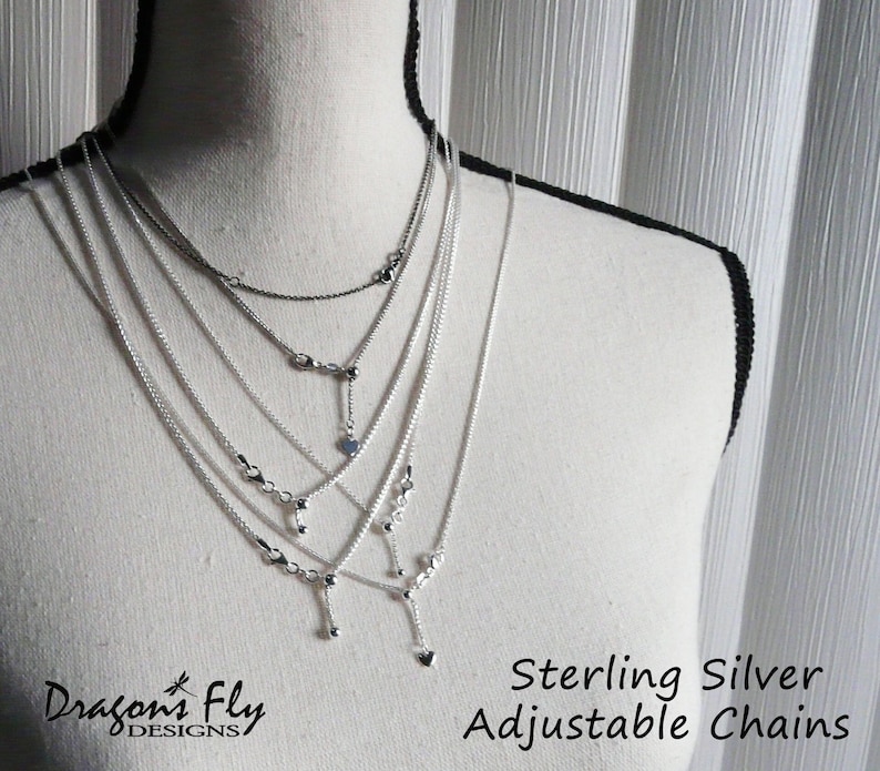 K&ouml;nnte beinhalten: Pr&auml;sentation von verstellbaren Ketten aus Sterlingsilber auf einer Schaufensterpuppe. Die Halsketten variieren in der L&auml;nge und weisen zarte Designs auf, darunter kleine Perlen und herzf&ouml;rmige Anh&auml;nger. Der Text "Sterling Silver Adjustable Chains" ist sichtbar.