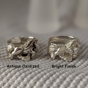 May include: Two silver rings with a detailed design of a horse running. The ring on the left has an antique oxidized finish, while the ring on the right has a bright finish. The rings are displayed on a gray fabric background.