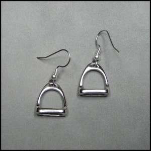 May include: A pair of silver stirrup earrings. The earrings are in the shape of a stirrup, with a small loop at the top for hanging. The earrings are a simple and elegant design.