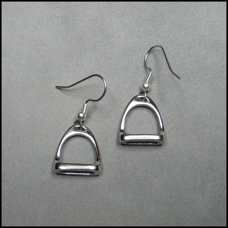 May include: A pair of silver stirrup earrings. The earrings are in the shape of a stirrup, with a small loop at the top for hanging. The earrings are a simple and elegant design.