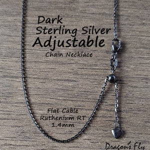 K&ouml;nnte beinhalten: Dunkle, verstellbare Kette aus Sterlingsilber. Die Halskette hat ein flaches Kabeldesign, eine Ruthenium-RT-Oberfl&auml;che und eine Dicke von 1,4 mm. Am Ende der verstellbaren Kette h&auml;ngt ein kleiner Herzanh&auml;nger.