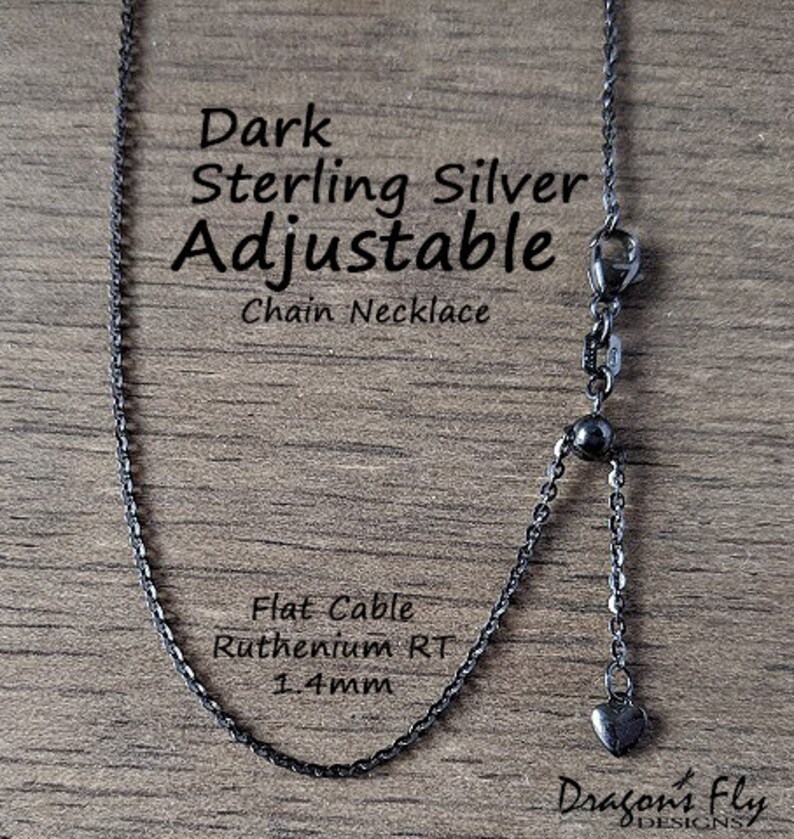 K&ouml;nnte beinhalten: Dunkle, verstellbare Kette aus Sterlingsilber. Die Halskette hat ein flaches Kabeldesign, eine Ruthenium-RT-Oberfl&auml;che und eine Dicke von 1,4 mm. Am Ende der verstellbaren Kette h&auml;ngt ein kleiner Herzanh&auml;nger.