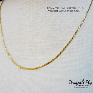 May include: A 1.5mm yellow glitter gold vermeil adjustable chain necklace. The chain is made of small, delicate links and has a subtle sparkle.  Dragonfly Designs is printed below the chain.