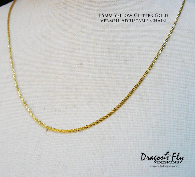 May include: A 1.5mm yellow glitter gold vermeil adjustable chain necklace. The chain is made of small, delicate links and has a subtle sparkle.  Dragonfly Designs is printed below the chain.