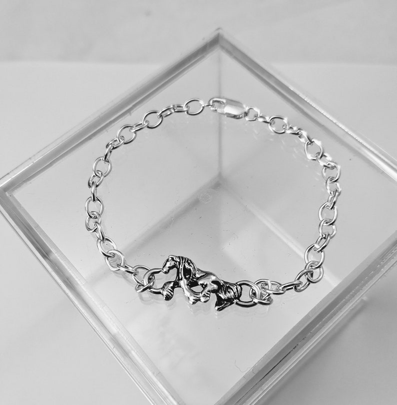 May include: A silver chain bracelet featuring a horse charm. The bracelet is made from a delicate chain and the horse charm is detailed and realistic.