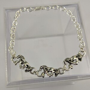May include: Silver chain bracelet featuring three horse charms. The charms are detailed and have a realistic look.