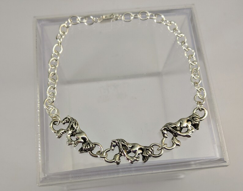 May include: Silver chain bracelet featuring three horse charms. The charms are detailed and have a realistic look.