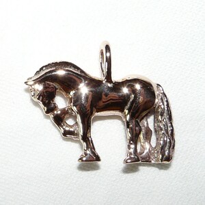 May include: A gold-toned horse charm pendant. The horse is standing on all four legs with its head lowered. The charm has a loop at the top for attaching to a necklace or bracelet.