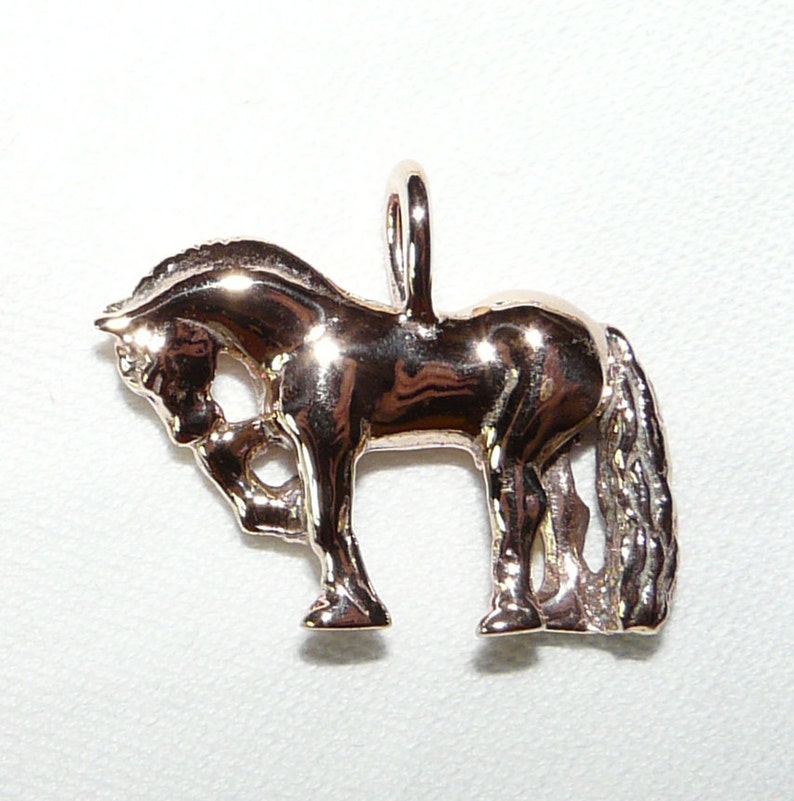 May include: A gold-toned horse charm pendant. The horse is standing on all four legs with its head lowered. The charm has a loop at the top for attaching to a necklace or bracelet.