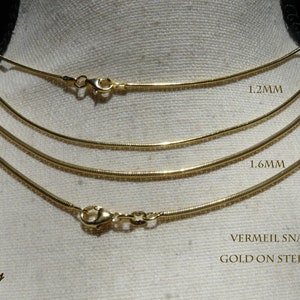 May include: Three gold vermeil snake chains on a white background. The chains are 1.2mm, 1.6mm, and 2mm wide. VERMEIL SNAKE CHAIN GOLD ON STERLING SILVER.