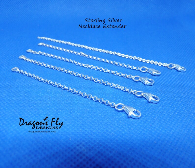 K&ouml;nnte beinhalten: F&uuml;nf silberne Kettenverl&auml;ngerungen auf blauem Hintergrund. Die Verl&auml;ngerungen bestehen aus einer zarten Kette mit einem Karabinerverschluss. Der Text "Sterling Silver Necklace Extender" befindet sich oben im Bild. Der Text "Dragonfly Designs" befindet sich unten im Bild.