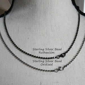 K&ouml;nnte beinhalten: Zwei Ketten aus Sterling-Silberperlen, eine oxidiert und eine mit einer Ruthenium-Beschichtung. Die Ketten werden auf einer wei&szlig;en Puppe pr&auml;sentiert.
