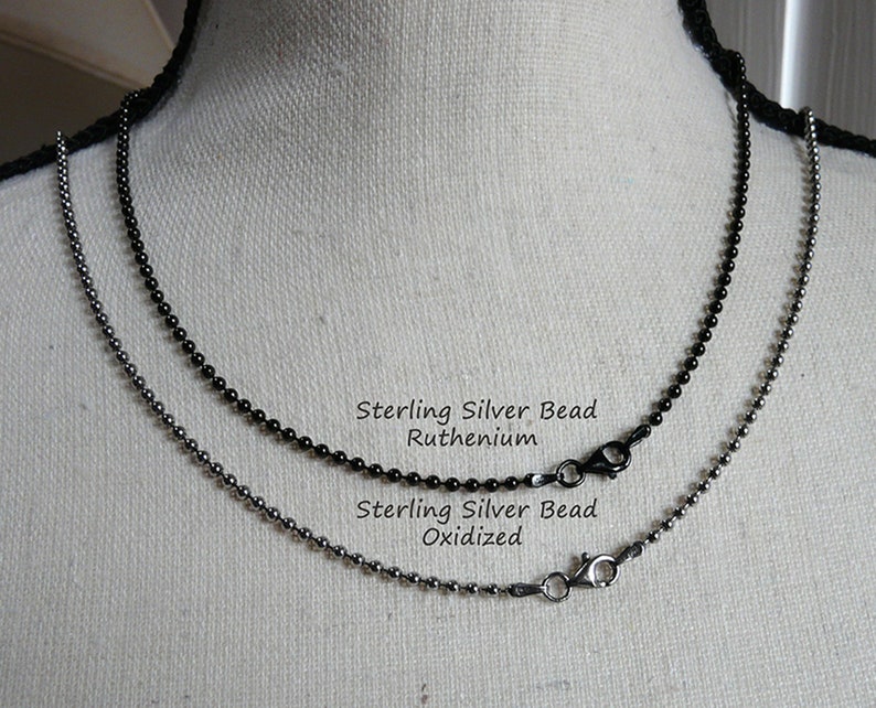 K&ouml;nnte beinhalten: Zwei Ketten aus Sterling-Silberperlen, eine oxidiert und eine mit einer Ruthenium-Beschichtung. Die Ketten werden auf einer wei&szlig;en Puppe pr&auml;sentiert.