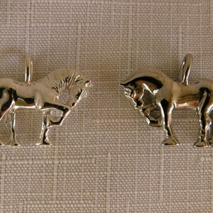 May include: Two silver horse charms, one standing and one lying down, both with detailed features.