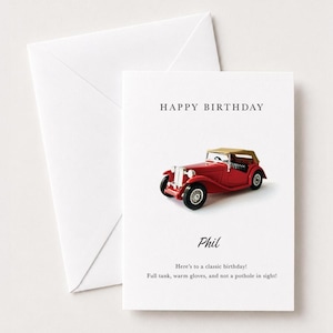 Op de afbeelding: Een witte wenskaart met een illustratie van een rode vintage cabriolet, de tekst HAPPY BIRTHDAY, de naam Phil en de boodschap: Here's to a classic birthday! Full tank, warm gloves, and not a pothole in sight! Inclusief een witte envelop.