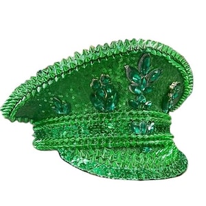 以下が含まれることがあります： エメラルド色の宝石のアクセントが付いた、グリーンのスパンコール付きミリタリースタイルの帽子。帽子にはつばがあり、スパンコールと尖ったトリムの列で装飾されています。帽子は鮮やかな緑色です。