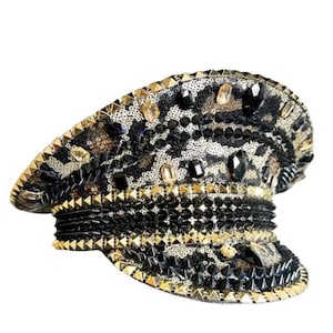 May include: A decorative leopard print hat with gold and black embellishments. The hat features a brim lined with gold studs, black and gold sequins, and large black and clear gemstones. The hat is a unique fashion accessory.