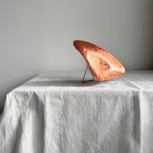 May include: A copper serving dish with a scalloped edge sits on a white linen tablecloth. The dish is angled and appears to be handmade.