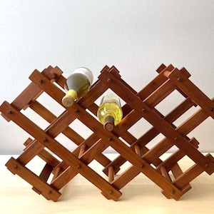 May include: A wooden wine rack with a lattice design, holding two bottles of wine. The rack is made of dark brown wood and has a folding, expandable design. The bottles are filled with a light-colored liquid.