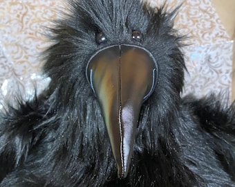 May include: A plush raven with black faux fur and a shiny black beak. The raven has small, round eyes and a detailed, textured appearance. The bird's feathers are soft and fluffy, creating a realistic look.