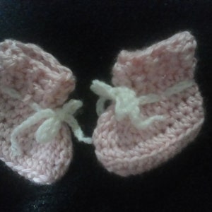 May include: A pair of pink crocheted baby booties with white crocheted ties.