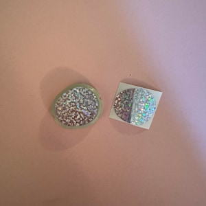 May include: Two round iridescent stickers with a holographic finish. The stickers are on a pink background.