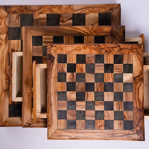 May include: A set of three wooden chess boards with drawers. The boards feature a checkerboard pattern in dark and light wood tones, framed by a decorative border. The drawers are open, revealing the interior.